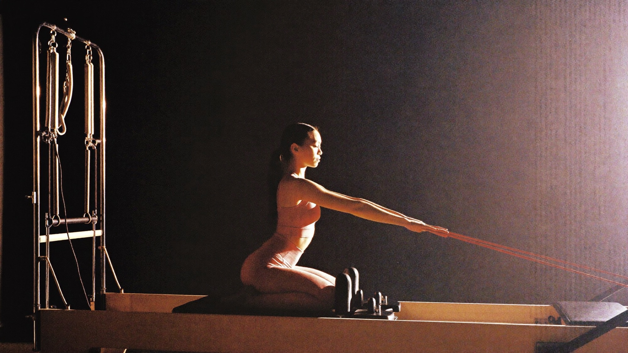 Woman kneeling on a Pilates reformer, drawing the straps